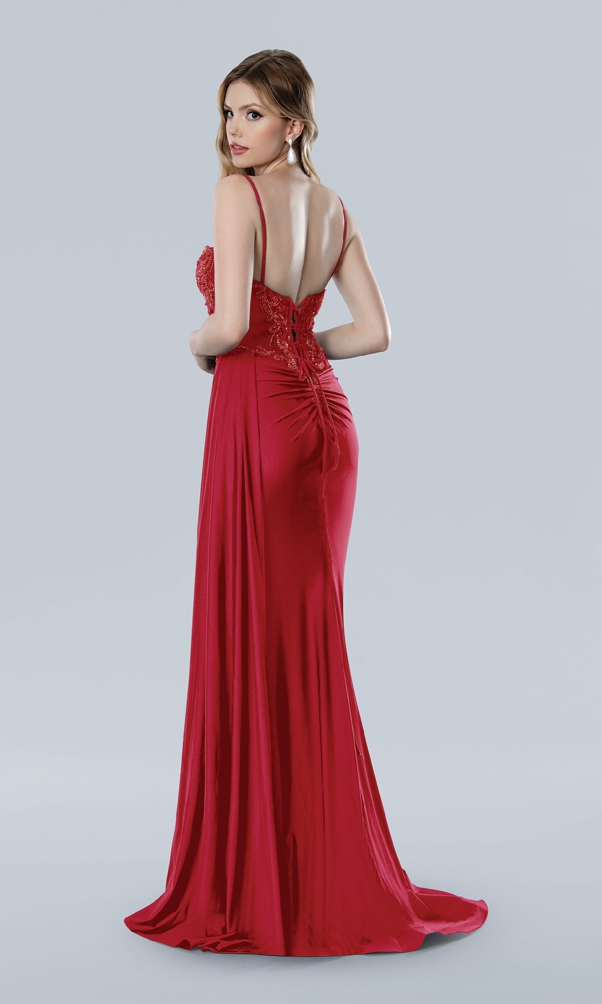 Model wears the Stella Couture 25224 long prom dress, showcasing an embellished sweetheart bodice, lace detailing, and a low lace-up back. She stands looking over her shoulder against a plain background.
